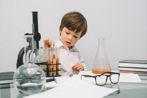 el chico con un microscopio y varios vistoso matraces en un blanco antecedentes. un chico haciendo experimentos en el laboratorio. explosión en el laboratorio. Ciencias y educación foto