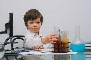 el chico con un microscopio y varios vistoso matraces en un blanco antecedentes. un chico haciendo experimentos en el laboratorio. explosión en el laboratorio. Ciencias y educación foto