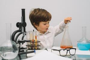 el chico con un microscopio y varios vistoso matraces en un blanco antecedentes. un chico haciendo experimentos en el laboratorio. explosión en el laboratorio. Ciencias y educación foto