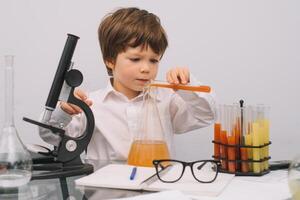 el chico con un microscopio y varios vistoso matraces en un blanco antecedentes. un chico haciendo experimentos en el laboratorio. explosión en el laboratorio. Ciencias y educación foto