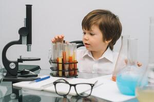 The boy with a microscope and various colorful flasks on a white background. A boy doing experiments in the laboratory. Explosion in the laboratory. Science and education photo