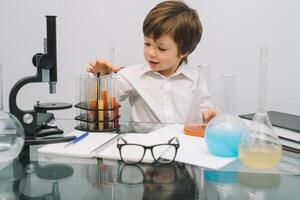 el chico con un microscopio y varios vistoso matraces en un blanco antecedentes. un chico haciendo experimentos en el laboratorio. explosión en el laboratorio. Ciencias y educación foto