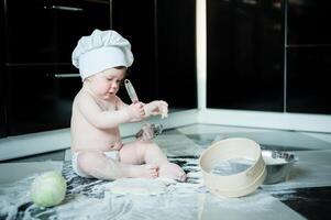 Little boy sitting on carpet in kitchen playing with cooking pots. Cute boy cooking in kitchen at home photo