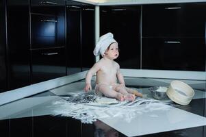 pequeño chico sentado en alfombra en cocina jugando con Cocinando ollas. linda chico Cocinando en cocina a hogar foto