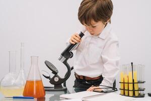 el chico con un microscopio y varios vistoso matraces en un blanco antecedentes. un chico haciendo experimentos en el laboratorio. explosión en el laboratorio. Ciencias y educación. foto