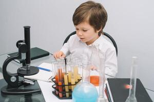 el chico con un microscopio y varios vistoso matraces en un blanco antecedentes. un chico haciendo experimentos en el laboratorio. explosión en el laboratorio. Ciencias y educación foto