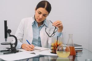 Beautiful medical doctors in gloves and glasses are working with substances in test tubes and microscope at the lab. Photo of attractive concentrated female doctor writing prescription on special form