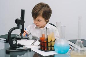 el chico con un microscopio y varios vistoso matraces en un blanco antecedentes. un chico haciendo experimentos en el laboratorio. explosión en el laboratorio. Ciencias y educación foto