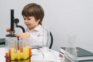 el chico con un microscopio y varios vistoso matraces en un blanco antecedentes. un chico haciendo experimentos en el laboratorio. explosión en el laboratorio. Ciencias y educación foto