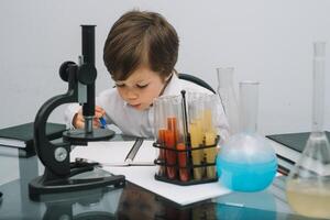 el chico con un microscopio y varios vistoso matraces en un blanco antecedentes. un chico haciendo experimentos en el laboratorio. explosión en el laboratorio. Ciencias y educación foto