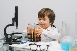 el chico con un microscopio y varios vistoso matraces en un blanco antecedentes. un chico haciendo experimentos en el laboratorio. explosión en el laboratorio. Ciencias y educación foto