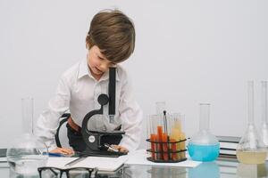 el chico con un microscopio y varios vistoso matraces en un blanco antecedentes. un chico haciendo experimentos en el laboratorio. explosión en el laboratorio. Ciencias y educación foto
