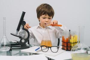 el chico con un microscopio y varios vistoso matraces en un blanco antecedentes. un chico haciendo experimentos en el laboratorio. explosión en el laboratorio. Ciencias y educación foto