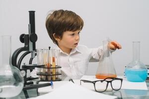 el chico con un microscopio y varios vistoso matraces en un blanco antecedentes. un chico haciendo experimentos en el laboratorio. explosión en el laboratorio. Ciencias y educación foto