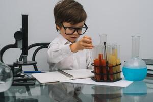 el chico con un microscopio y varios vistoso matraces en un blanco antecedentes. un chico haciendo experimentos en el laboratorio. explosión en el laboratorio. Ciencias y educación foto