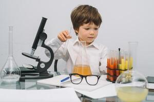 The boy with a microscope and various colorful flasks on a white background. A boy doing experiments in the laboratory. Explosion in the laboratory. Science and education photo