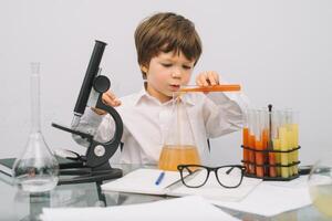 el chico con un microscopio y varios vistoso matraces en un blanco antecedentes. un chico haciendo experimentos en el laboratorio. explosión en el laboratorio. Ciencias y educación foto