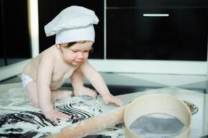 pequeño chico sentado en alfombra en cocina jugando con Cocinando ollas. linda chico Cocinando en cocina a hogar foto