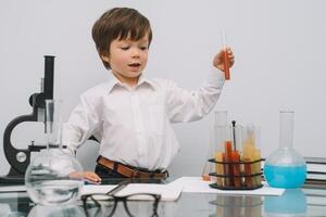 The boy with a microscope and various colorful flasks on a white background. A boy doing experiments in the laboratory. Explosion in the laboratory. Science and education photo