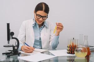 Beautiful medical doctors in gloves and glasses are working with substances in test tubes and microscope at the lab. Photo of attractive concentrated female doctor writing prescription on special form