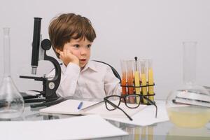 The boy with a microscope and various colorful flasks on a white background. A boy doing experiments in the laboratory. Explosion in the laboratory. Science and education photo