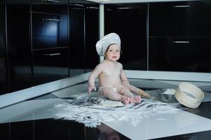 Little boy sitting on carpet in kitchen playing with cooking pots. Cute boy cooking in kitchen at home photo