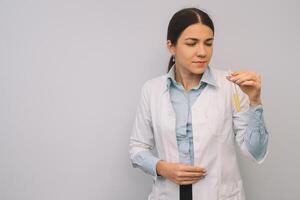 Female doctor in white uniform is holding flasks while standing against white background. photo