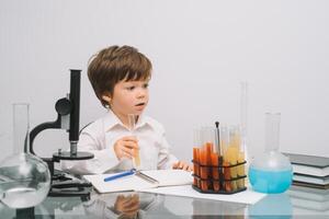 el chico con un microscopio y varios vistoso matraces en un blanco antecedentes. un chico haciendo experimentos en el laboratorio. explosión en el laboratorio. Ciencias y educación foto