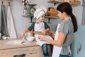 joven contento mamá y su bebé cocinar galletas a hogar en el cocina. Navidad hecho en casa pan de jengibre. linda chico con madre en blanco uniforme y sombrero cocido chocolate galletas foto