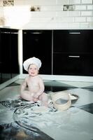 Little boy sitting on carpet in kitchen playing with cooking pots. Cute boy cooking in kitchen at home photo