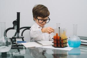 el chico con un microscopio y varios vistoso matraces en un blanco antecedentes. un chico haciendo experimentos en el laboratorio. explosión en el laboratorio. Ciencias y educación foto