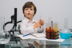 el chico con un microscopio y varios vistoso matraces en un blanco antecedentes. un chico haciendo experimentos en el laboratorio. explosión en el laboratorio. Ciencias y educación foto