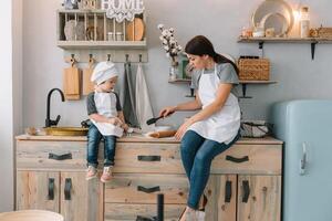 Young happy mom and her baby cook cookies at home in the kitchen. Christmas Homemade Gingerbread. cute boy with mother in white uniform and hat cooked chocolate cookies photo