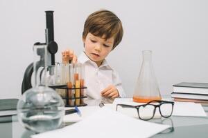 el chico con un microscopio y varios vistoso matraces en un blanco antecedentes. un chico haciendo experimentos en el laboratorio. explosión en el laboratorio. Ciencias y educación foto