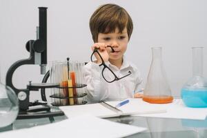 el chico con un microscopio y varios vistoso matraces en un blanco antecedentes. un chico haciendo experimentos en el laboratorio. explosión en el laboratorio. Ciencias y educación foto