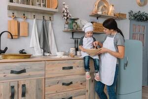 Young happy mom and her baby cook cookies at home in the kitchen. Christmas Homemade Gingerbread. cute boy with mother in white uniform and hat cooked chocolate cookies photo