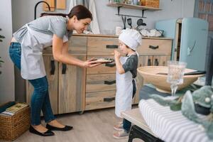 Young happy mom and her baby cook cookies at home in the kitchen. Christmas Homemade Gingerbread. cute boy with mother in white uniform and hat cooked chocolate cookies photo