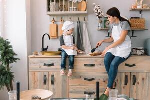 Young happy mom and her baby cook cookies at home in the kitchen. Christmas Homemade Gingerbread. cute boy with mother in white uniform and hat cooked chocolate cookies photo