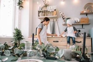 Young happy mom and her baby cook cookies at home in the kitchen. Christmas Homemade Gingerbread. cute boy with mother in white uniform and hat cooked chocolate cookies. photo