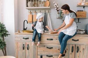 Young happy mom and her baby cook cookies at home in the kitchen. Christmas Homemade Gingerbread. cute boy with mother in white uniform and hat cooked chocolate cookies photo