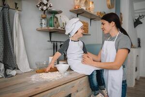 Young happy mom and her baby cook cookies at home in the kitchen. Christmas Homemade Gingerbread. cute boy with mother in white uniform and hat cooked chocolate cookies photo