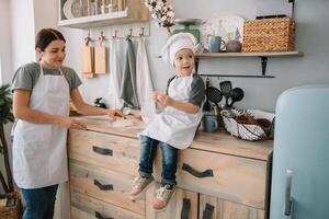 Young happy mom and her baby cook cookies at home in the kitchen. Christmas Homemade Gingerbread. cute boy with mother in white uniform and hat cooked chocolate cookies. photo