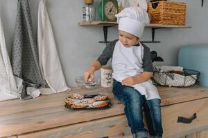 Young happy mom and her baby cook cookies at home in the kitchen. Christmas Homemade Gingerbread. cute boy with mother in white uniform and hat cooked chocolate cookies photo