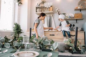 Young happy mom and her baby cook cookies at home in the kitchen. Christmas Homemade Gingerbread. cute boy with mother in white uniform and hat cooked chocolate cookies. photo