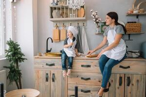 Young happy mom and her baby cook cookies at home in the kitchen. Christmas Homemade Gingerbread. cute boy with mother in white uniform and hat cooked chocolate cookies photo