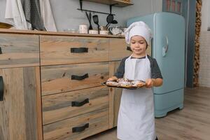 Young boy cute on the kitchen cook chef in white uniform and hat near table. Christmas homemade gingerbread. the boy cooked the chocolate cookies photo