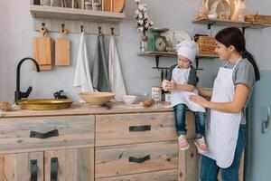 Young happy mom and her baby cook cookies at home in the kitchen. Christmas Homemade Gingerbread. cute boy with mother in white uniform and hat cooked chocolate cookies photo