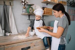 Young happy mom and her baby cook cookies at home in the kitchen. Christmas Homemade Gingerbread. cute boy with mother in white uniform and hat cooked chocolate cookies photo