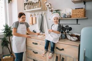 Young happy mom and her baby cook cookies at home in the kitchen. Christmas Homemade Gingerbread. cute boy with mother in white uniform and hat cooked chocolate cookies. photo