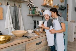 Young happy mom and her baby cook cookies at home in the kitchen. Christmas Homemade Gingerbread. cute boy with mother in white uniform and hat cooked chocolate cookies photo